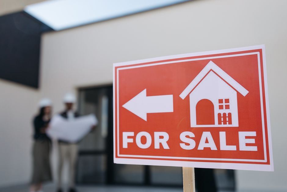 A red for sale sign in front of a home, representing a property that could be targeted by deed fraud
