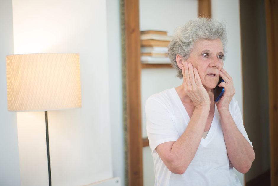 An older woman with white hair talking on the phone with a concerned look on her face