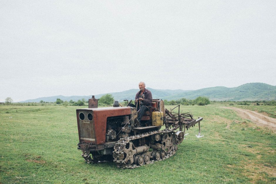 An older man driving a tractor across a rural field